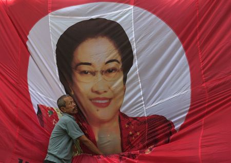 インドネシアのメガワティ元大統領は、ジョコ政権の複数の閣僚に対し辞任しないよう忠告したことを明らかにした。写真はメガワティ元大統領の垂れ幕を整える男性。ジャカルタで１４年２月撮影。（2024年 ロイター/Beawiharta/File Photo）