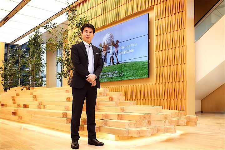 「武田グローバル本社」の受付がある４階フロア。福富康浩経営企画部長兼社長室長の背景にあるのは国産ヒノキの無垢材で作られたベンチ。
