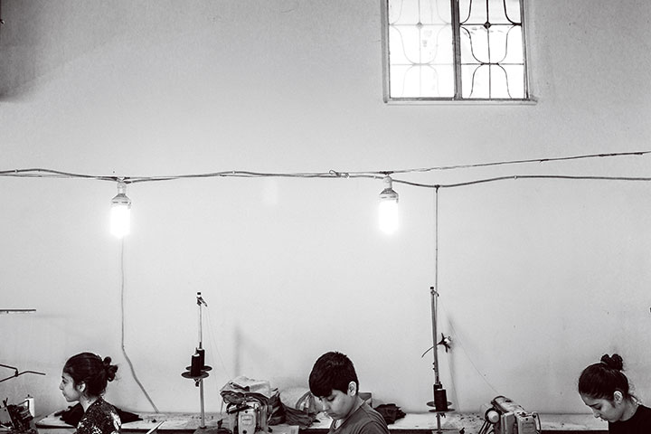 ＜ゼイネップ（12、写真左端）＞トルコ南部のメルシンの織物工場で集中して機械に向かうゼイネップは、シリア北部のコバニ（アインアルアラブ）から逃れて1年以上になる。父は別の作業場でアイロンがけを、彼女はパジャマにポケットを縫い付ける仕事をして4人のきょうだいを養う。週に6日、1日10時間の労働で、毎日約3000のポケットを縫い付ける。シリアで通った学校のことを問うと、こらえ切れずに涙を流した。「ここでは働くしかない。父を支えなければ家族が生活できない」