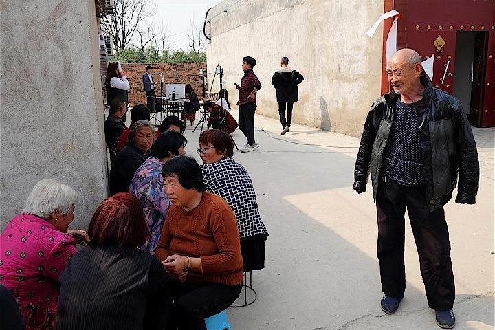 犬が吠え、鶏が歩き回るなかで、住民が未舗装の道路沿いに並び、自分たちの顔の画像と引き替えに、ヤカンやポット、ティーカップを手に入れている。写真は河南省の村で3月20日撮影（2019年　ロイター/Cate Cadell）