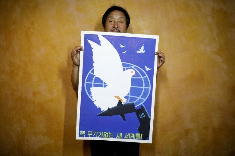 北朝鮮のプロパガンダポスターを見せるギャラリー責任者。「核兵器なき新世界に向けて！」とある。ソウルで８月撮影（２０１７年　ロイター/Kim Hong-Ji）