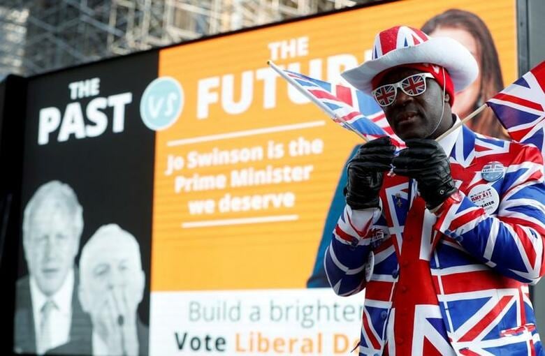 英国が欧州連合（EU）から離脱する予定だった10月31日、EU離脱の命運を握る12月12日の総選挙に向けて本格的な選挙戦がスタートした。写真は自由民主党の選挙ポスターの前に立つ離脱支持者。10月31日、ロンドンで撮影（2019年　ロイター/Yara Nardi）