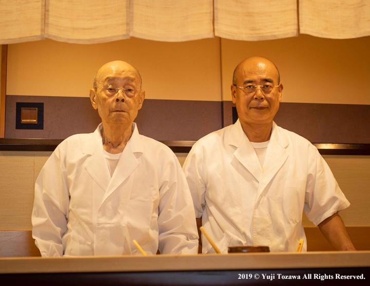 94歳になった今も現役の小野二郎氏（左）と、その姿を近くで見続けてきた長男の禎一氏（『「すきやばし次郎」　小野禎一 父と私の60年』より。撮影：戸澤裕司）
