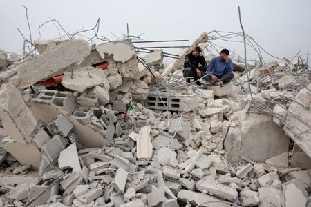 2月9日、ヨルダン川西岸ラマラ近郊の町で、破壊された建物のがれきの上に座るパレスチナ人男性ら。REUTERS/Mohammed Torokman