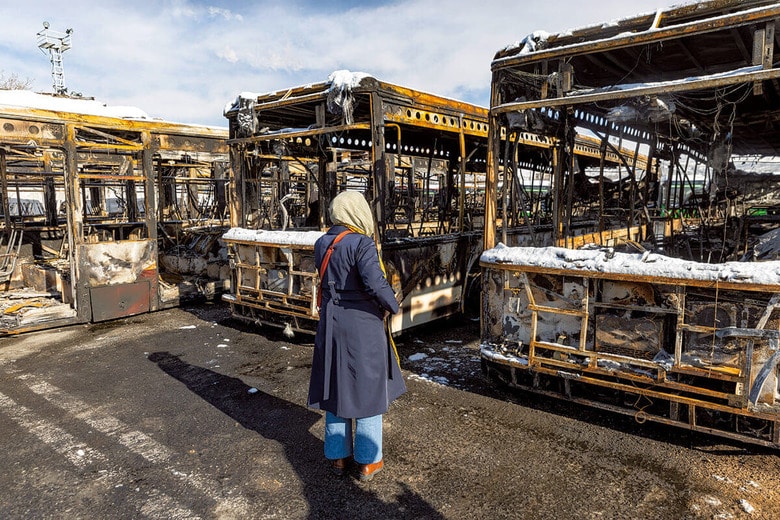 1月21日、抗議デモが弾圧された首都テヘランで焼け焦げたバスを見つめる女性。政府はこうした現場をデモ隊の仕業として公開した　MAJID SAEEDI/GETTY IMAGES