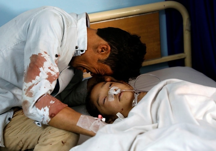 自爆テロで負傷した少女の枕元で泣く男性（カブール、4月22日）　Mohammad Ismail-REUTERS