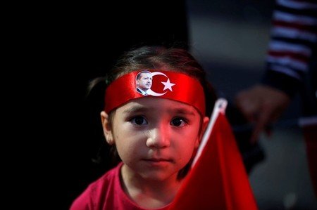 　７月１９日、トルコ軍兵士によるクーデター未遂の危機に瀕したエルドアン大統領だが、敵を打ち破り、すぐさま復権を宣言した。だがこのクーデター未遂によって、混乱する国内の対立はさらに深まりつつある。大統領の顔写真付きの鉢巻を巻いた少女。トルコ首都アンカラでの政府支持者のデモで２０日撮影（２０１６年　ロイター/Baz Ratner）
