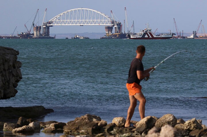 ケルチ海峡に面するクリミアの海岸で釣りをする男性。遠くに見えるのは、ロシアとクリミアを陸路で結ぶためロシアが建設中の橋　Pavel Rebrov-REUTERS