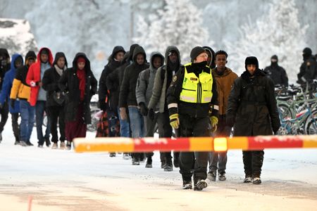 フィンランドのオルポ首相は２４日、ロシアは意図的に難民申請希望者をフィランドに送り込む「ハイブリッド攻撃」をやめるべきと非難した。写真は１１月２３日、フィンランド北部の国境の検問所で移民を先導するフィンランドの国境警備隊（２０２３年　ロイター／Lehtikuva/Jussi Nukari via REUTERS）