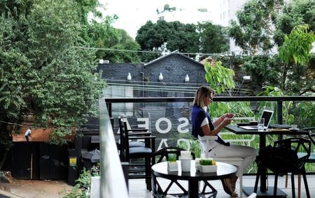 　７月２７日、  ポルトガルの首都リスボン中心部。６月のある朝、営業スペシャリストのビクトール・ソトさん（３３）はカフェのテラスに座り、欧州から米州まで世界中の同僚と連絡を取り合いながら仕事に励んでいた。写真はサンパウロのカフェでパソコンを使って作業する女性。２０１７年１０月撮影（２０２２年　ロイター/Nacho Doce）
