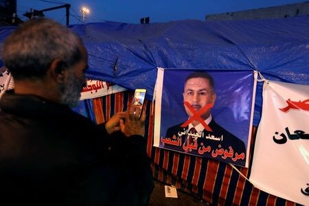 １２月２６日、イラクのサレハ大統領は、親イラン派の国会勢力が推す人物を首相に指名することを拒否し、大統領を辞任する用意があると表明した。写真はバグダッドで政党連合が新首相候補として推すバスラ県のエイダニ知事のポスターの写真を撮る抗議活動参加者（２０１９年　ロイター/Khalid al-Mousily）
