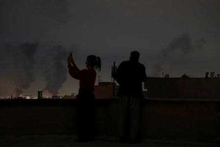 3月7日、イランのテヘランで、爆発後に煙が上がる中、携帯電話を捜査する女性。REUTERS/WANA