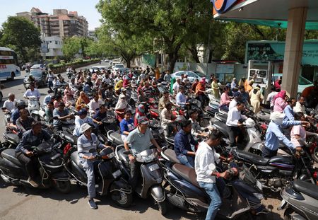 　３月２７日、インド政府は、イラン戦争に伴う国際原油価格の変動を受け、ガソリン・軽油の物品税を引き下げる一方、航空燃料や軽油の輸出に対し超過利得税を導入した。写真は、米・イスラエルとイランの紛争が続く中、供給途絶への懸念から二輪車にガソリンを給油しようと列を作る人々。インドのアーメダバードで３月撮影（２０２６年　ロイター/Amit Dave ）