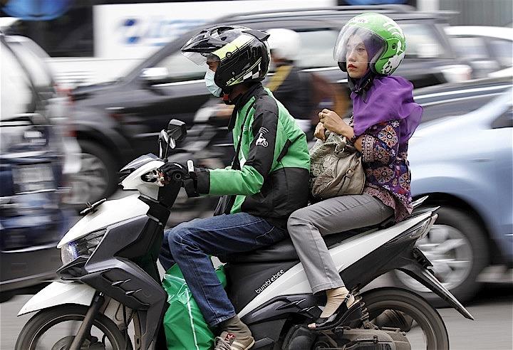物流とサービスをマルチ展開して急成長するGOJEK。写真はジャカルタ市内で女性客を乗せて走るGOJEK。Garry Lotulung - REUTERS