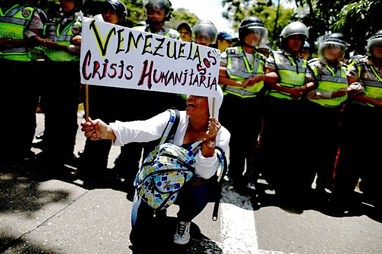 警官隊の前で「ベネズエラSOS、人道主義の危機」と書いたプラカードを掲げる女性（2016年　ロイター／Carlos Garcia Rawlings）