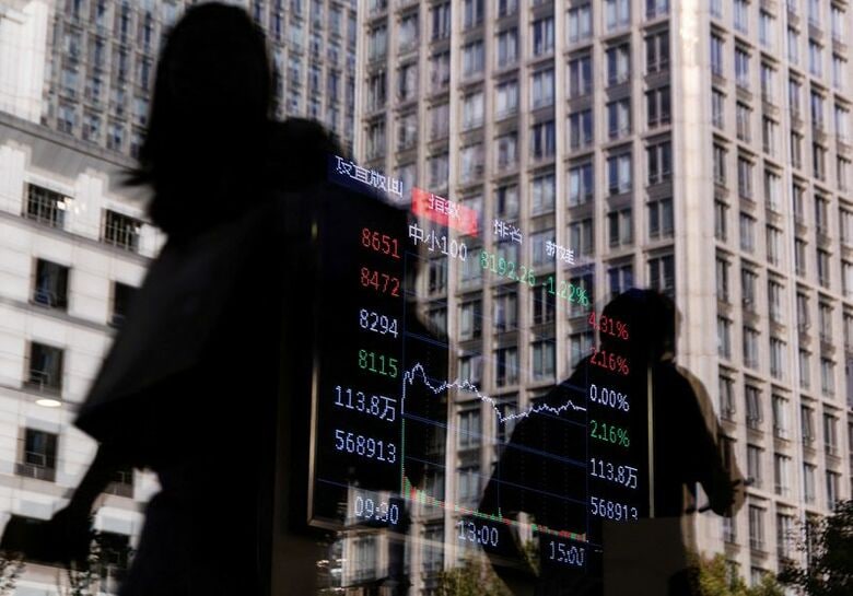 写真は株価指数のグラフが表示された証券会社の電子掲示板の前を通る人々。中国・北京で昨年10月撮影。REUTERS/Maxim Shemetov