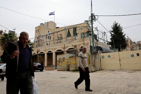 2月9日、イスラエルが占領するヨルダン川西岸地区ヘブロンにあるイスラエル入植地の前を歩くパレスチナの人々。REUTERS/Mussa Qawasma